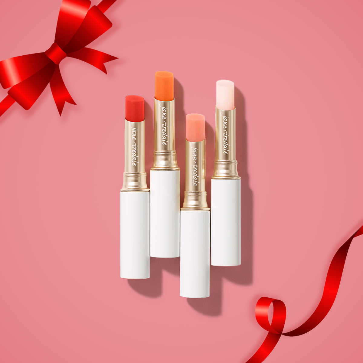 Ein Produktbild des jane iredale Mineral Make-up Produktes Just Kissed Lip and Cheek Stain auf einem rosafarbenen Hintergrund und mit einer Schleife in der oberen linken Ecke des Bildes.